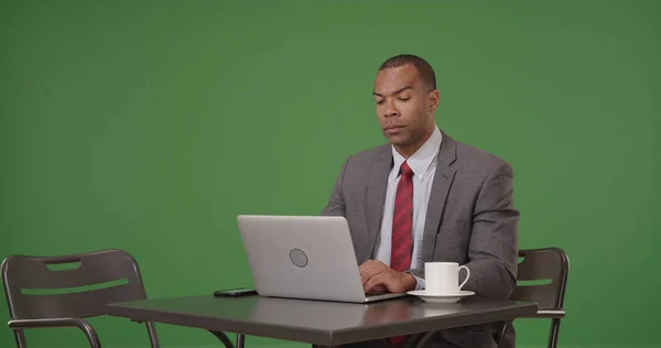 一个拿着咖啡的黑人商人在他的笔记本电脑上的绿色屏幕上工作 — 图库照片