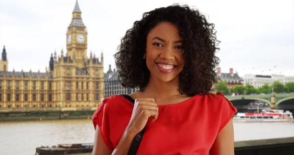Happy young black woman smiling to camera across view of Big Ben in London