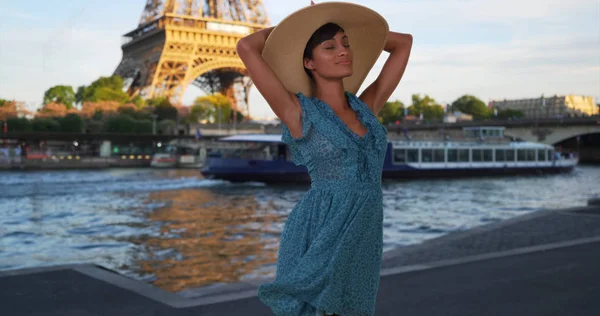 Mixed race female tourist moves with joy next to Seine River near Eiffel Tower