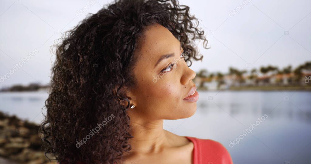 Thoughtful African-American young lady looking around near rocky coast