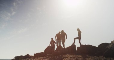 Plajda kayalar üzerinde yürüyen arkadaşlar