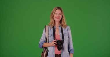 Orta gülümseyen yaşlı beyaz bir kadın yeşil ekranda dijital kamera tutarak