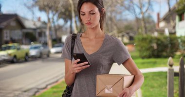 Konut kaldırımda posta paket tutarken cep telefonu kullanan kadın