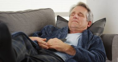 Bir tablet tutan bir kanepede uyuyan olgun adam
