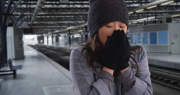 Close up of Asian millennial wearing beanie and mittens at train station