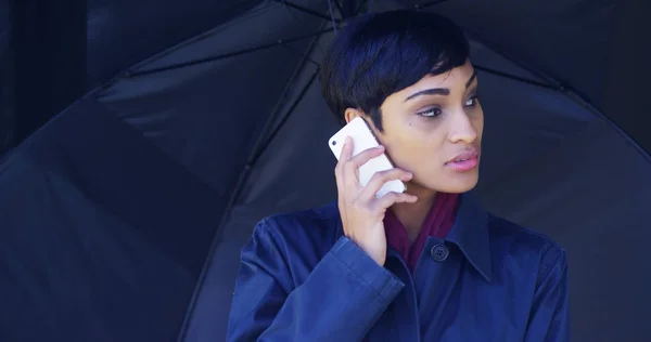 African woman stuck in rain storm trying to make phone call