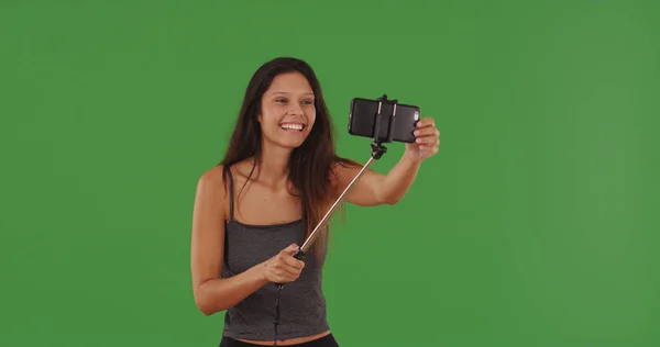千禧一代女孩使用手机与自拍棒采取自拍在绿色屏幕上 — 图库照片