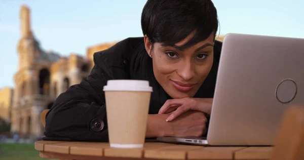 Stunning black woman with laptop stares intently at camera near Roman Colosseum