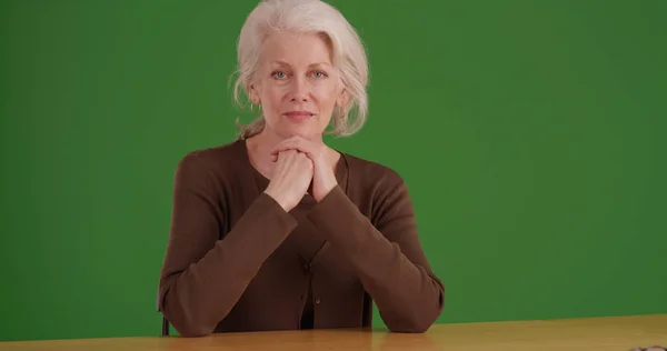可爱的老白种人妇女坐在办公桌上看着绿色屏幕上的相机 — 图库照片