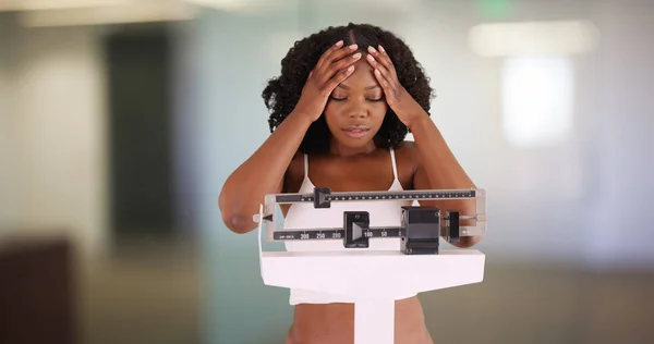 Unhappy young woman weighs herself scale frustrated with weight gain
