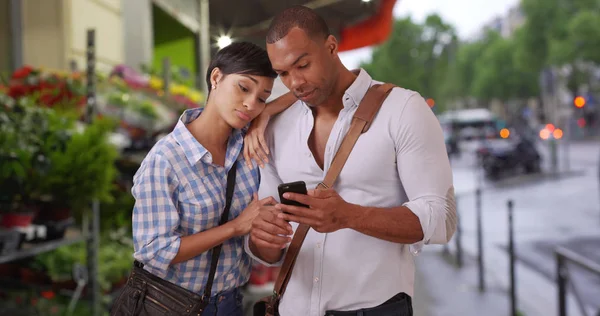 Young black couple in city watch smartphone outside on sidewalk