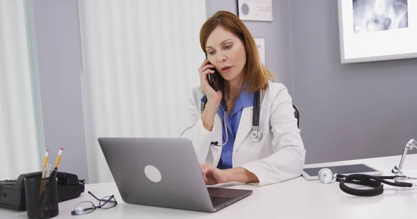 Attractive Mid Aged Doctor Using Latop Computer While Talking Smartphone — Stock Photo, Image