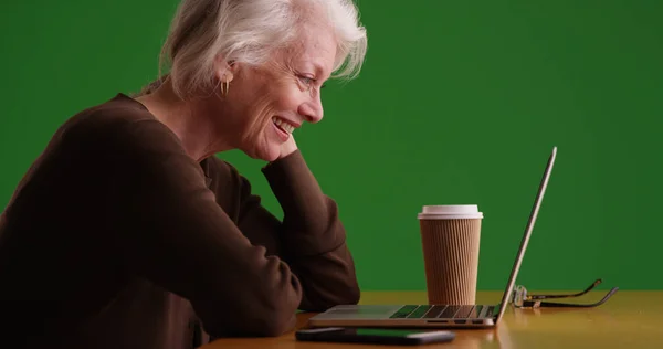 在绿色屏幕上观看笔记本电脑上有趣的视频的开朗成熟的妇女的个人资料 — 图库照片