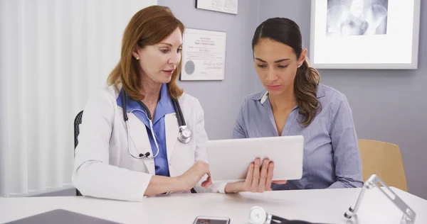 Senior medical physician using tablet to share lab results with young patient