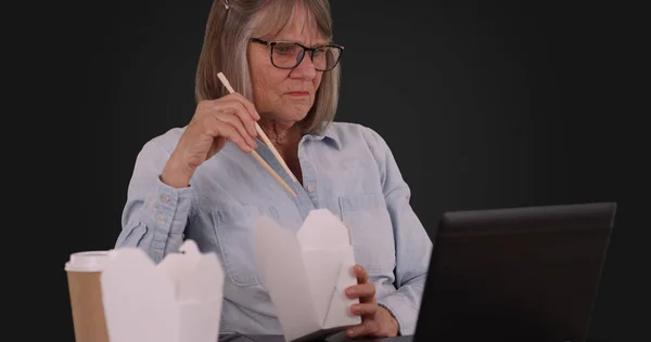 昼食と灰色の背景にラップトップ コンピューターを使用して引退した年配の女性 — ストック写真