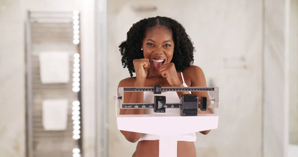 Cute smiling black female stands on weight scale cheering weight loss