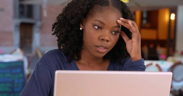 Unhappy black woman has to work on vacation uses laptop at cafe in Rome