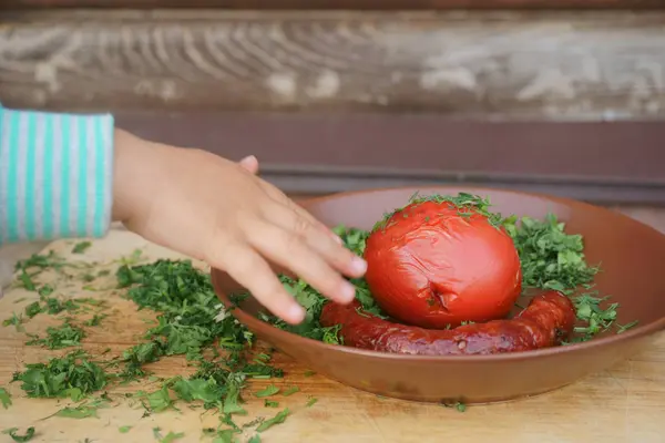 Salsichas grelhadas e tomates com verduras, as mãos das crianças tiram comida do prato — Fotografia de Stock