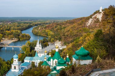 Dağın yamacında bir manastır. Nehrin yakınındaki ormanda küçük bir kilise. Nehrin üzerinde mavi gökyüzü. Dağdaki bir askerin anıtı.