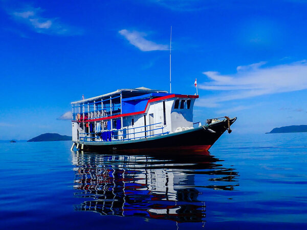 Diving boat with reflection in the water and beautiful blue sky and islands in the background