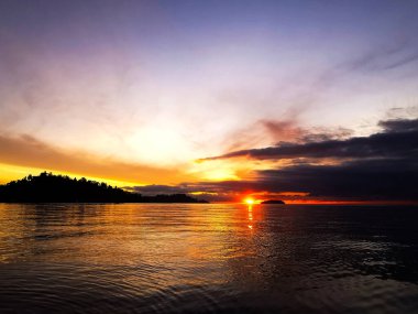 Güneşin güzel manzarası ufukta adalar ve önplandaki okyanusla birlikte yükseliyor.