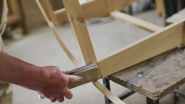 Elderly man carpenter builds a small boat with his hands out of wood in a small workshop — Stock Video