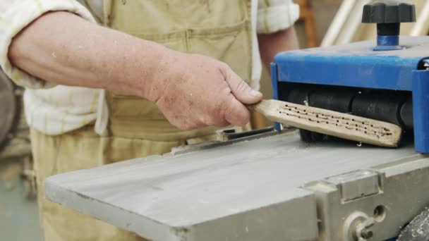 Ηλικιωμένος άνδρας ξυλουργός χτίζει μια μικρή βάρκα με τα χέρια του από το ξύλο σε ένα μικρό εργαστήριο — Αρχείο Βίντεο