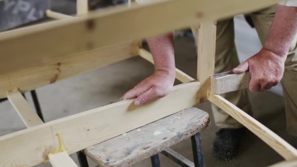 Ein älterer Tischler baut in einer kleinen Werkstatt mit seinen Händen aus Holz ein kleines Boot — Stockvideo