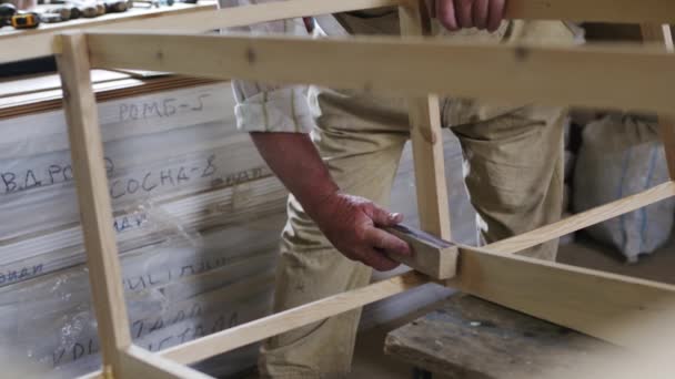 Uomo anziano falegname costruisce una piccola barca con le mani di legno in una piccola officina — Video Stock