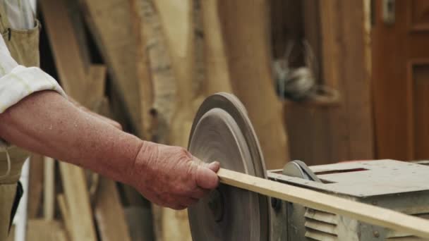 Oudere man timmerman bouwt een klein bootje met zijn handen van hout in een kleine werkplaats — Stockvideo