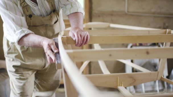 Anciano carpintero construye un pequeño barco con las manos de madera en un pequeño taller — Vídeos de Stock
