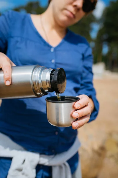 Vrouw gieten hete thee uit een thermoskan op een zandstrand op een zonnige dag. Close-up. — Stockfoto