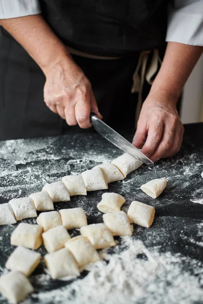 Las manos de las mujeres cortan la masa en trozos con cuchillo de cocina — Foto de Stock