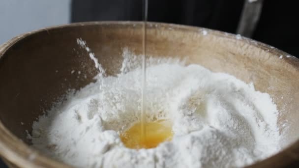 Egg falls on wooden bowl with flour. — Stock Video