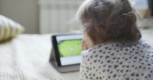 Child lying on his stomach on the bed watching cartoons on the tablet — Stock Video