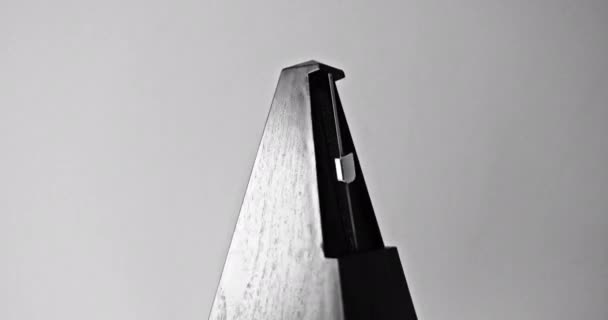 Close-up shot van vintage metronoom met slinger slaat traag ritme op de grijze achtergrond — Stockvideo