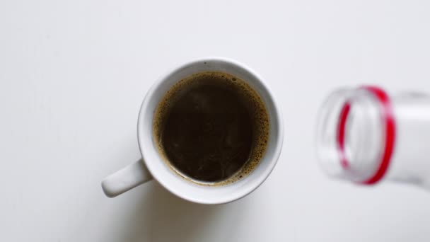 Выливать молоко из бутылки в чашку черного кофе . — стоковое видео