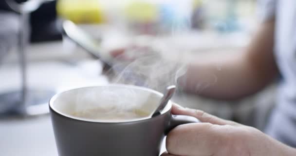 Homem se senta à mesa com smartphone e bebe bebida quente fresca — Vídeo de Stock