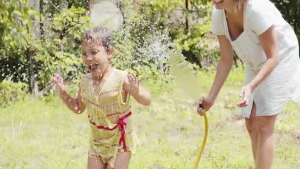 Kleines Mädchen tanzt unter der Gischt aus einem Gartenschlauch — Stockvideo