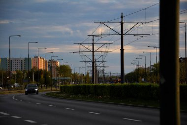 Varşova Polonya 'da ilkbaharda yoldaki siyah araba, doğa yeşil ve parlak, gökyüzü açık, bir tramvay ve binalar görebilirsiniz.