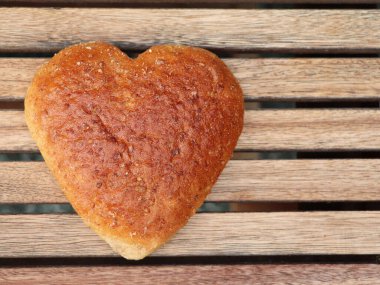Kalp şeklinde ekmek ahşap bir masanın üzerinde yatıyor. Lezzetli aromatik sağlıklı ekmek Almanya 'dan. Çavdar ekmeği ve hecelenmiş undan yapılan ekmek. Sağlıklı zayıflatıcı.