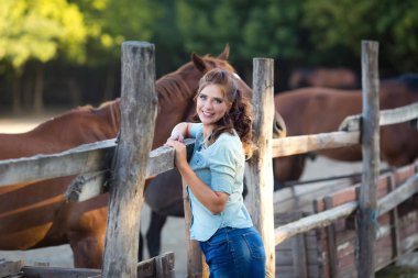 Atları ile istikrarlı, kot giymiş kıvırcık saçlı genç gülümseyen kadın