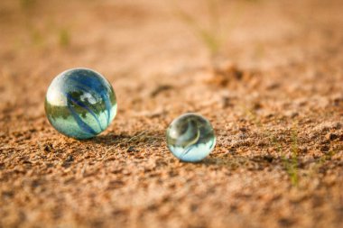 Kumlu bir zeminde iki bilye görebilirsiniz.