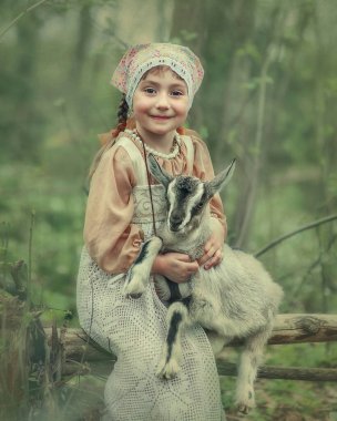 Küçük bir çocuk keçi çocuğunu kucaklıyor. Kız çok mutlu. Ormanda keçi çobanı olan bir kızın portresi.
