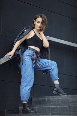 Mavi kotlu, siyah bluzlu ve ceketli kız merdivenlerde. Deri ceketli güzel bir kadının portresi. Şehir tarzı.