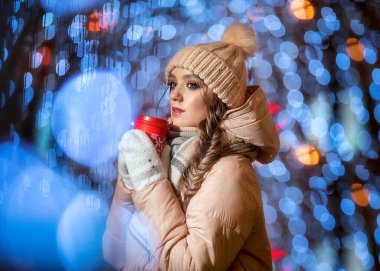 Eldivenli genç bir bayan ve arka planda Noel çelenklerinden bir şapka. Güzel bir kızın kış portresi. Unutulmaz bir Noel gecesi Bir fincan kahveyle.