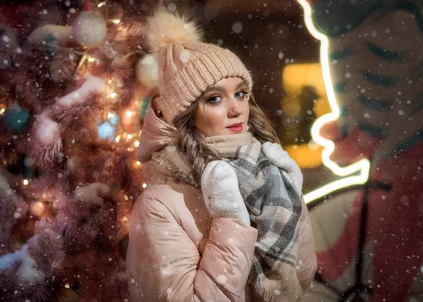 Eldivenli genç bir kadın ve pembe bir Noel ağacının yanında bir şapka. Bej ceketli güzel bir kızın kış portresi. Bir bayanın Noel portresi.