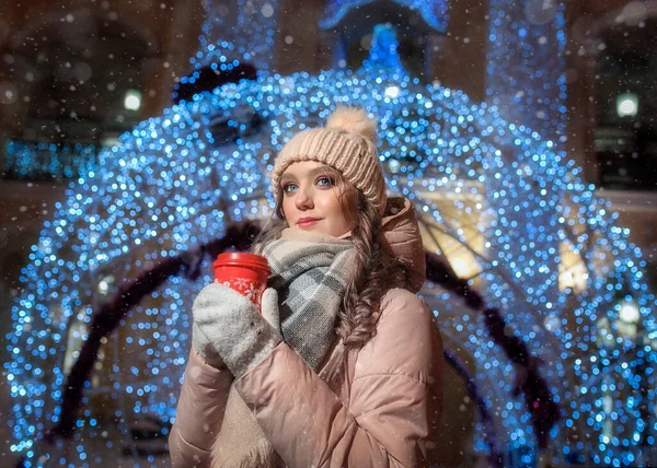 Büyük bir Noel balosunun arka planında genç bir bayan. Güzel bir kızın kış portresi. Bir kış gecesinde elinde bir fincan kahveyle bir kızın portresi..