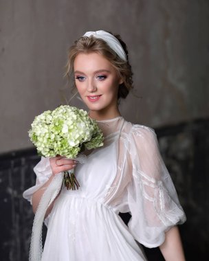 Stüdyoda lüks bir gelinlik içinde ince, güzel bir kadın. Elinde beyaz bir buketle gelinin portresi..