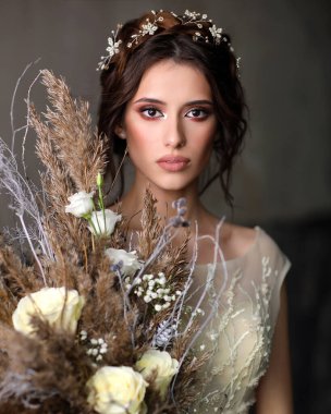 Kafasında beyaz bir çelenk ve elinde buket olan gelin..